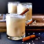 Mexican Horchata in glasses with cinnamon sticks in them. They are sitting on a black surface