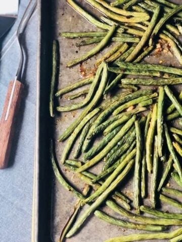 green beans on a roasting pan with a spatula on the counter next to it