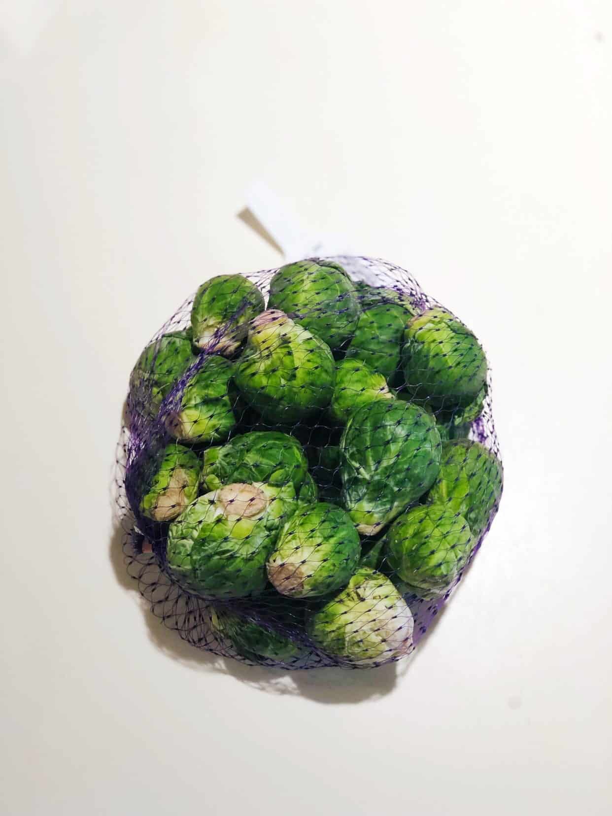 Mesh bag of Brussels sprouts on a white surface.