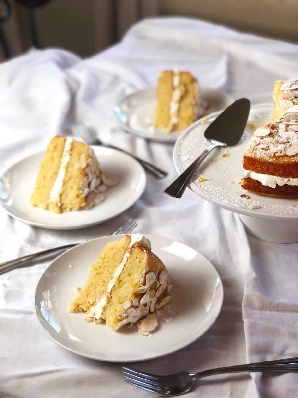 Vanilla almond layer cake sliced up on individual plates with the cake on a cake stand next to them.