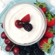 A small glass bowl of dip surrounded by fruit