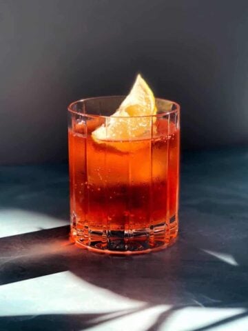 Aperol and soda in glass with a lemon wedge on a blue counter
