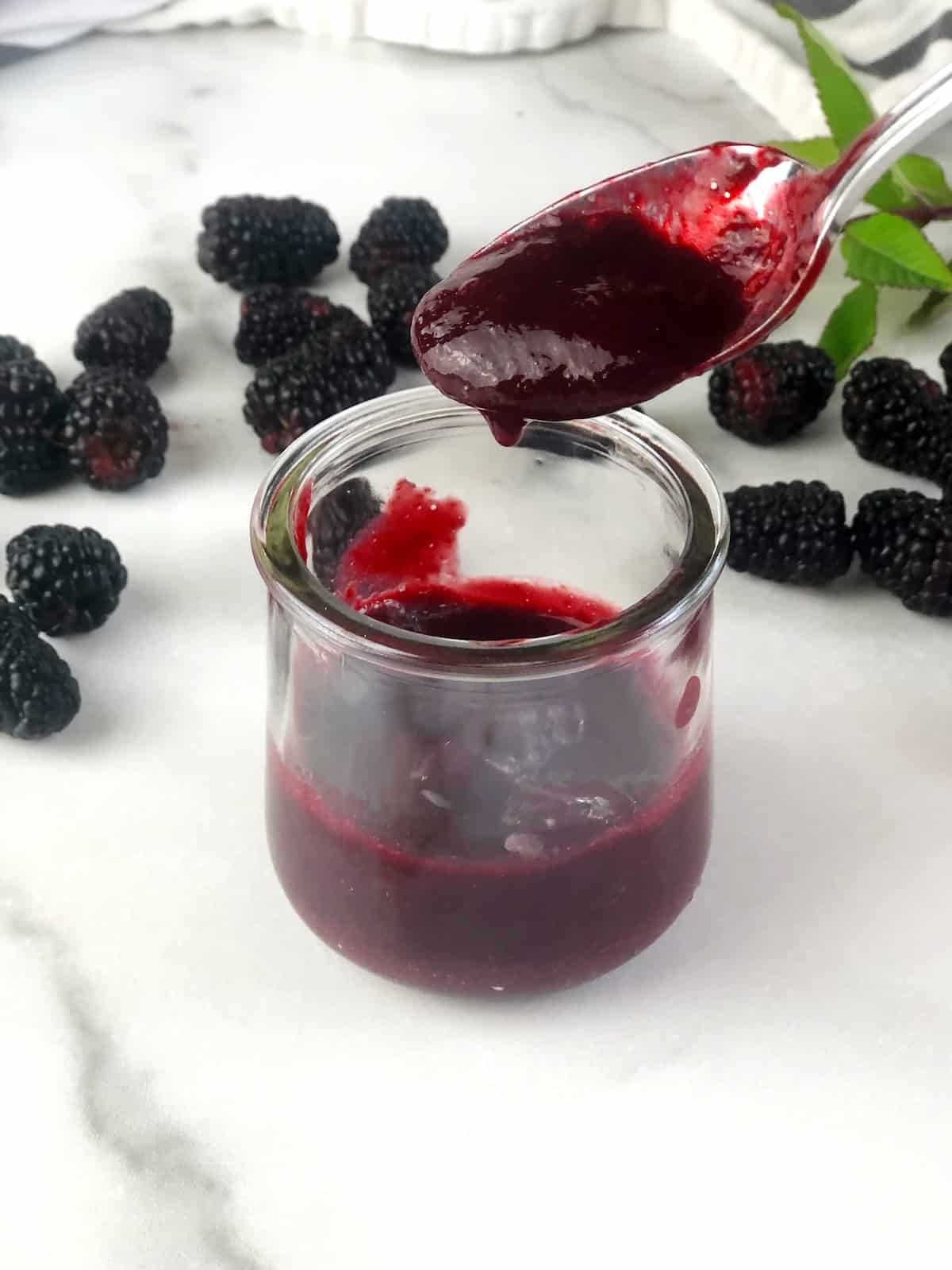 closeup of blackberry puree being poured off of spoon into a bowl