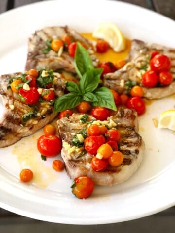 grilled pork chops on plate with tomatoes on top