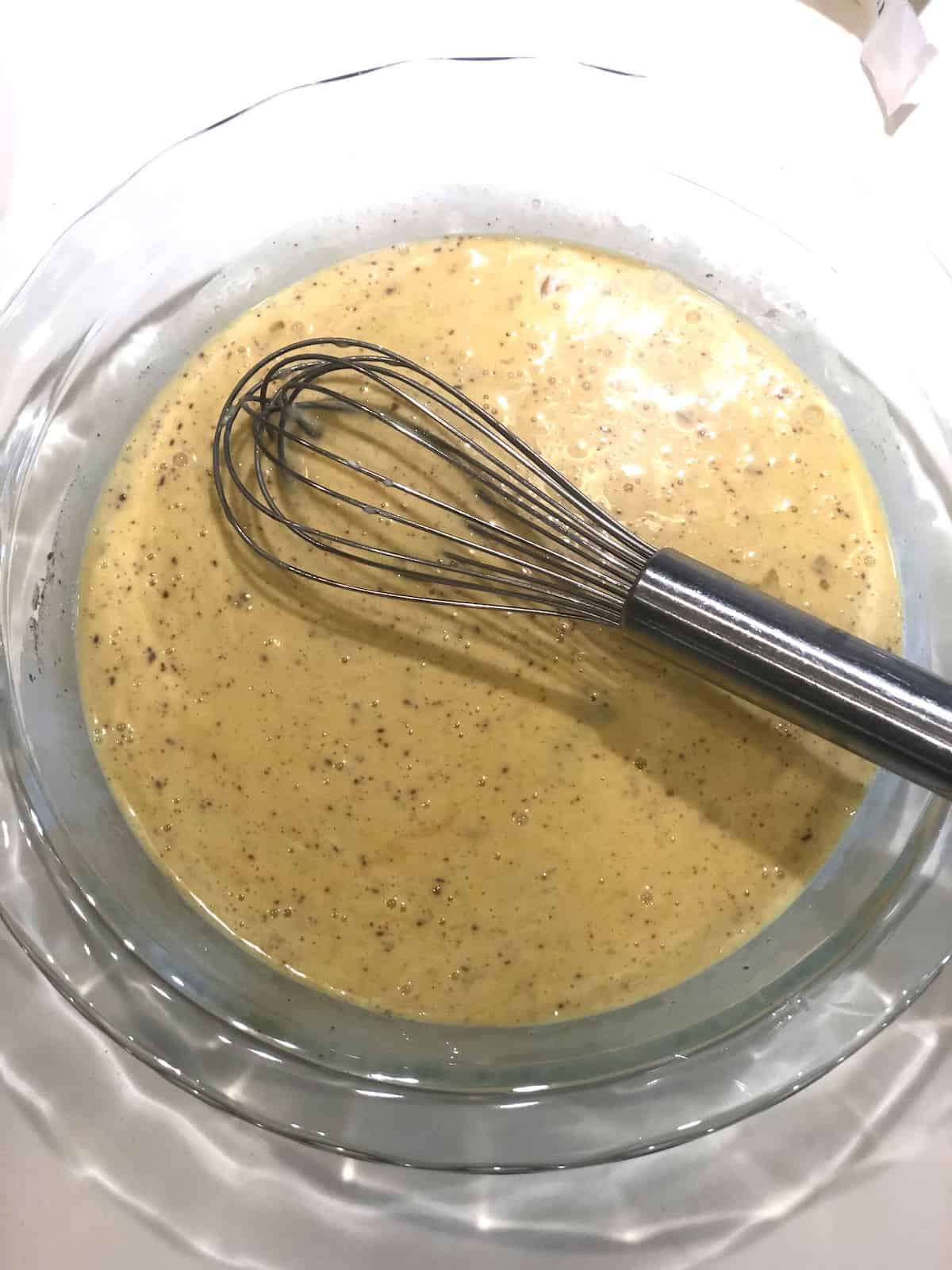 A bowl of egg mixture with a whisk in it.