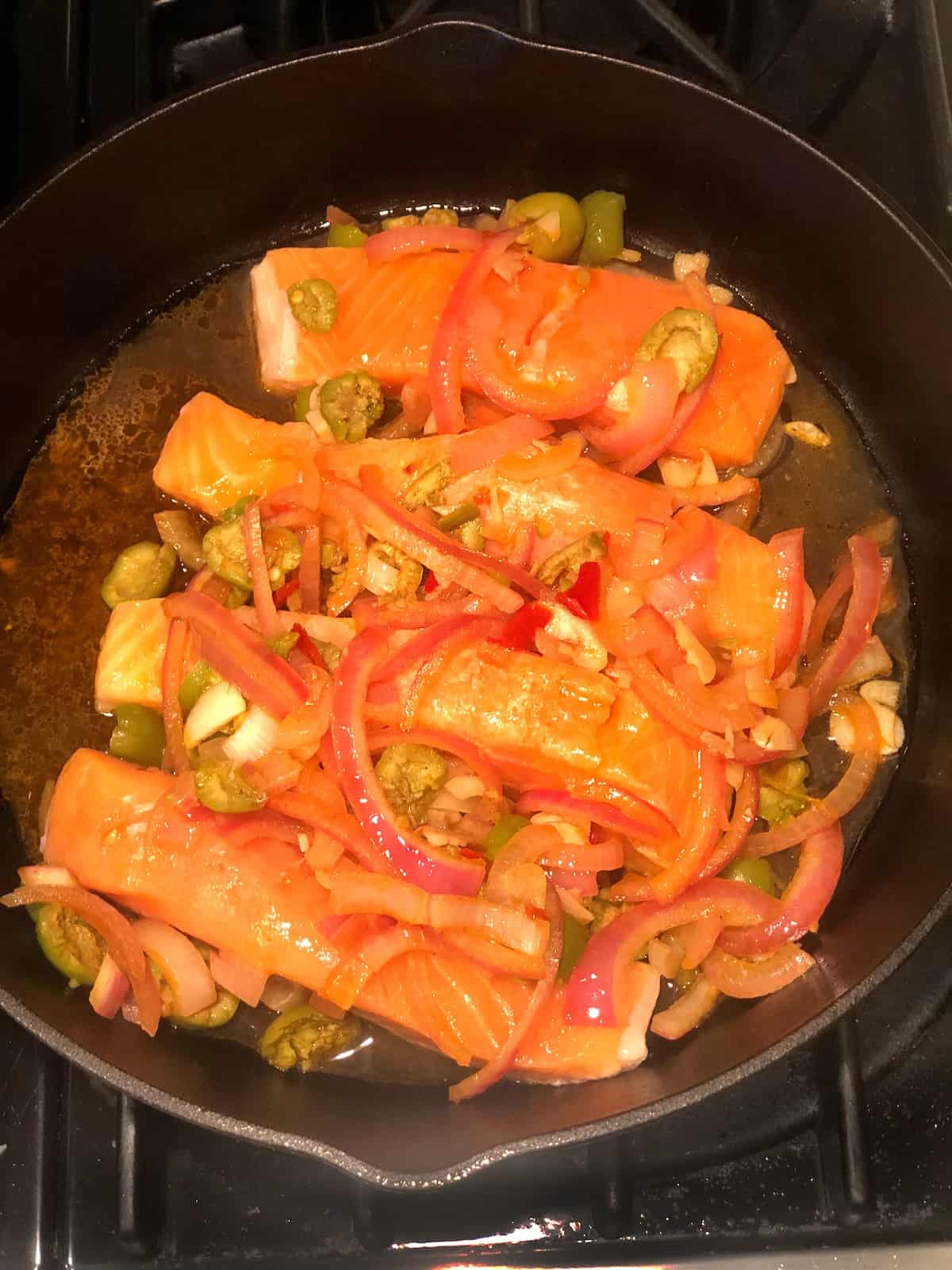 Salmon in a skillet with onions and olives.
