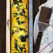 A quiche with spinach and cheese on a white plate.