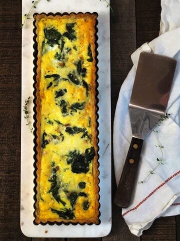 A quiche with spinach and cheese on a white plate.
