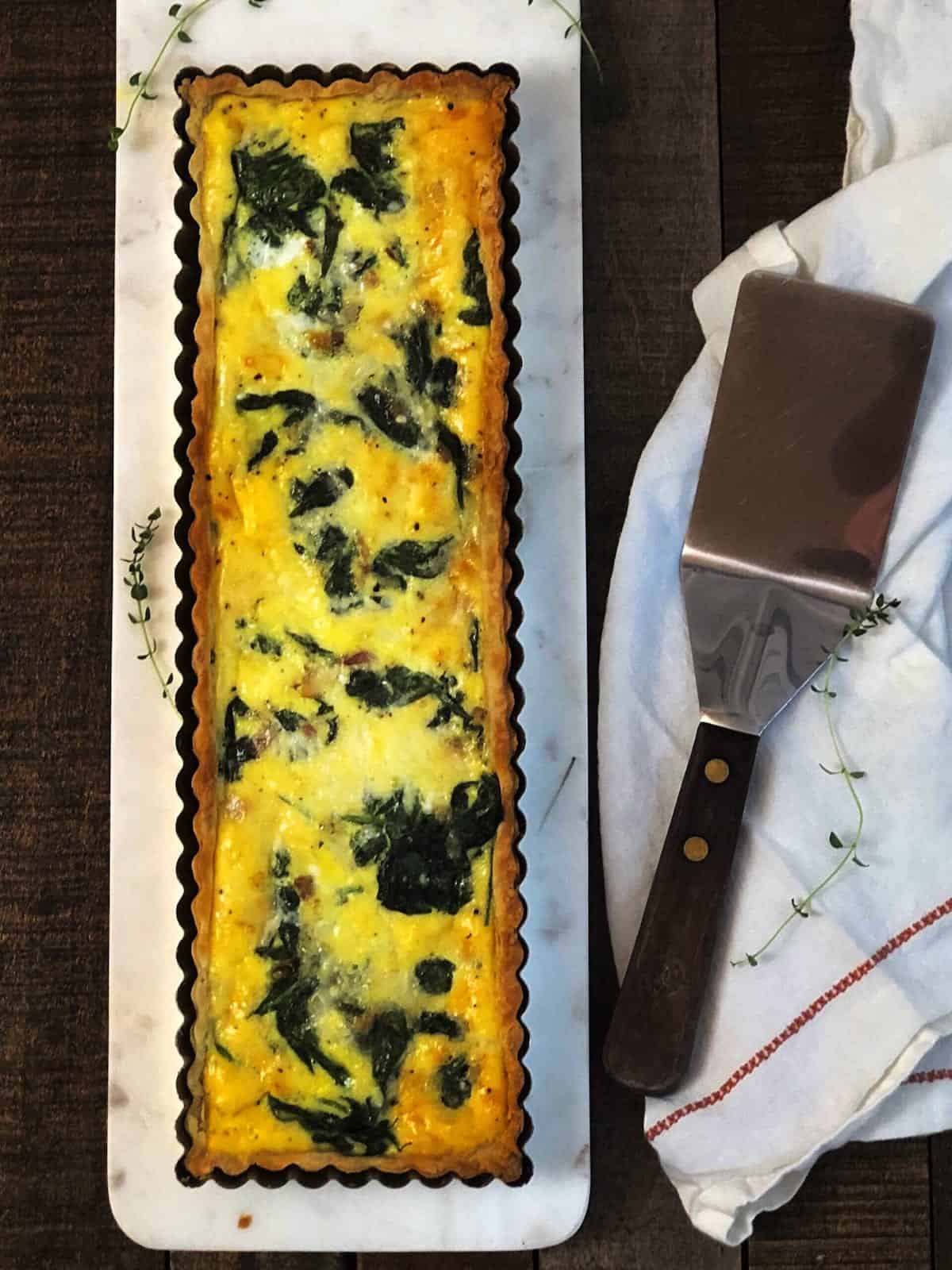 A quiche with spinach and cheese on a white plate.