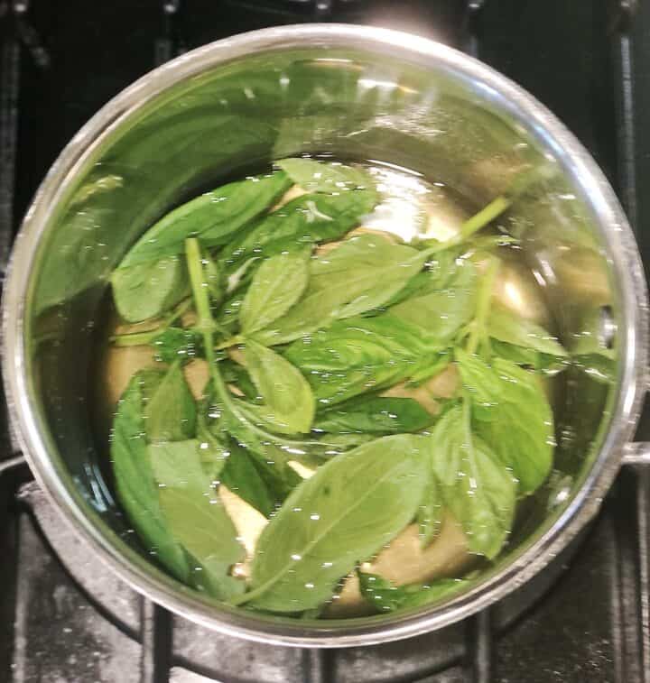 A pot with basil leaves on top of a stove.