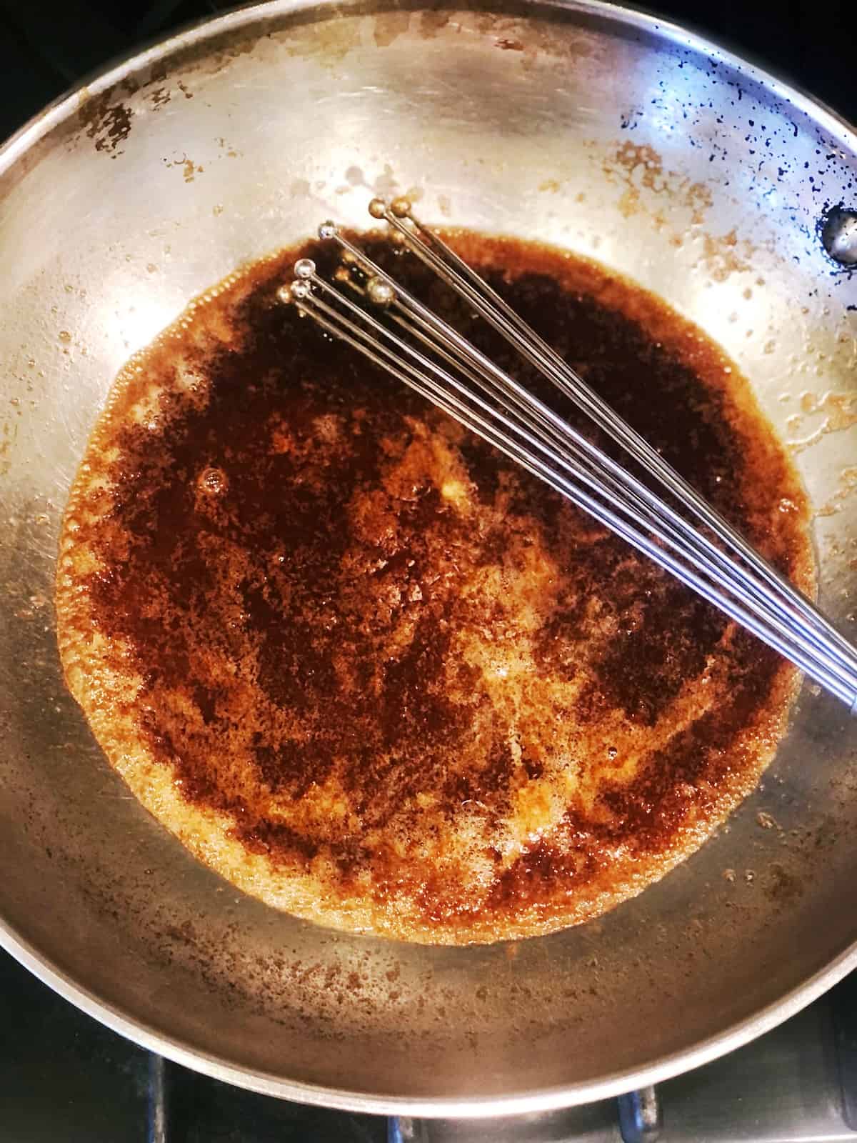 A wok filled with a brown sauce on top of a stove.