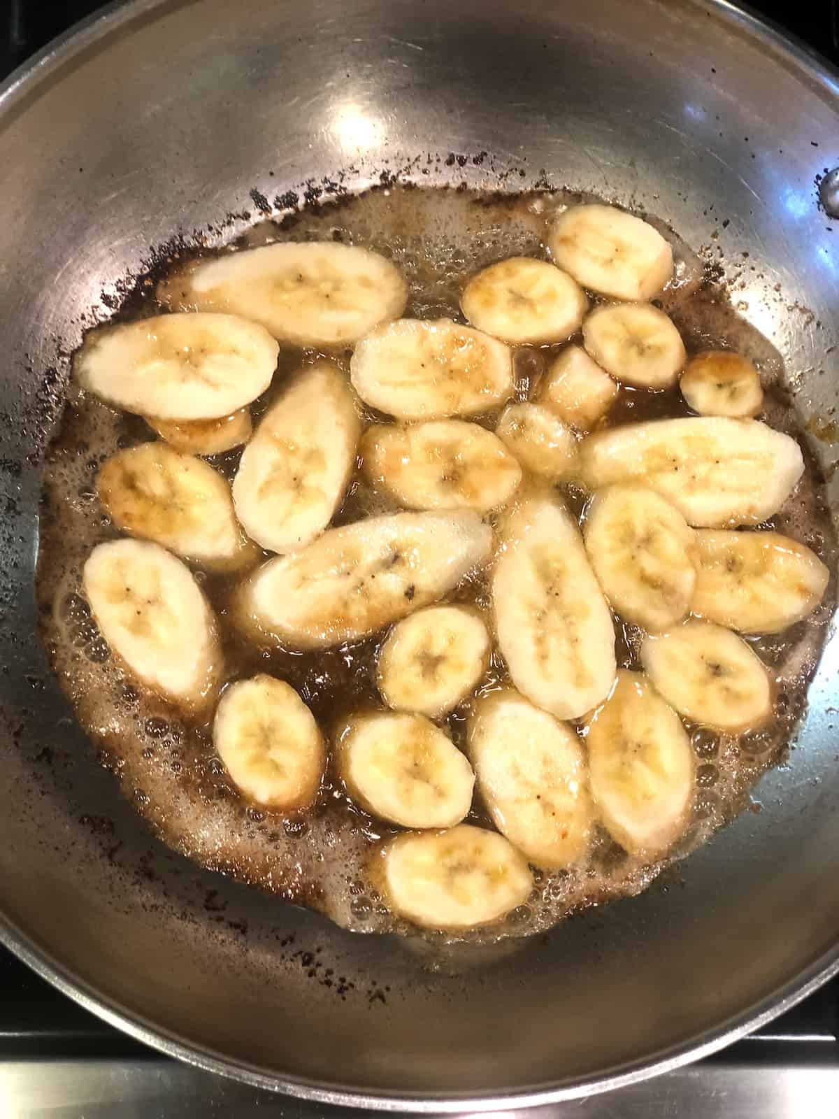 A frying pan with banana slices, butter, and sugar in it.