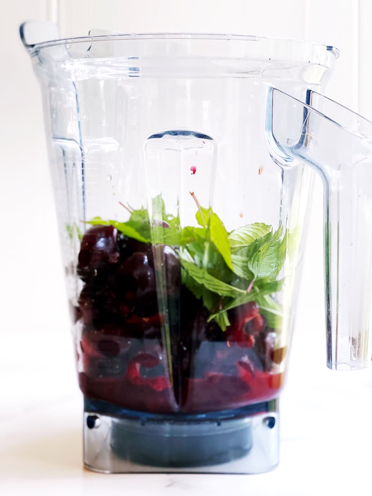 A blender filled with cherries and mint.
