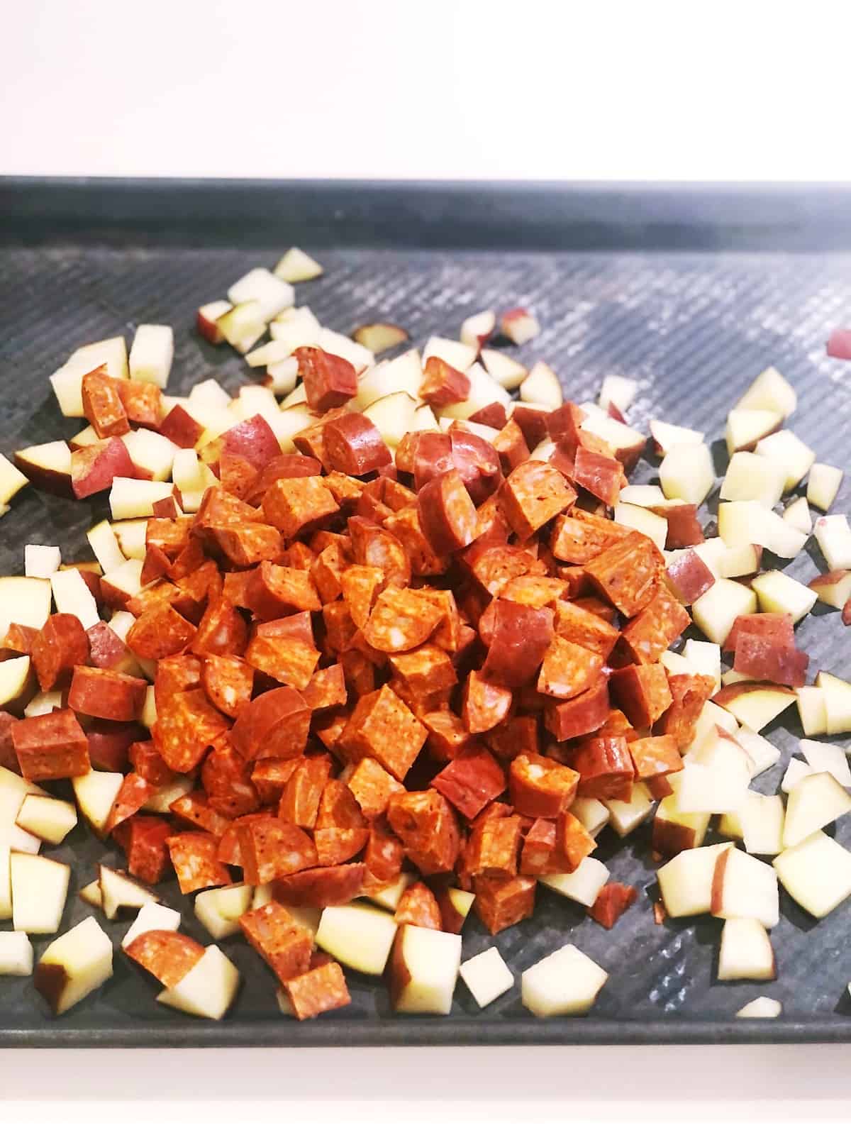 Chopped chorizo and potatoes on a baking sheet.