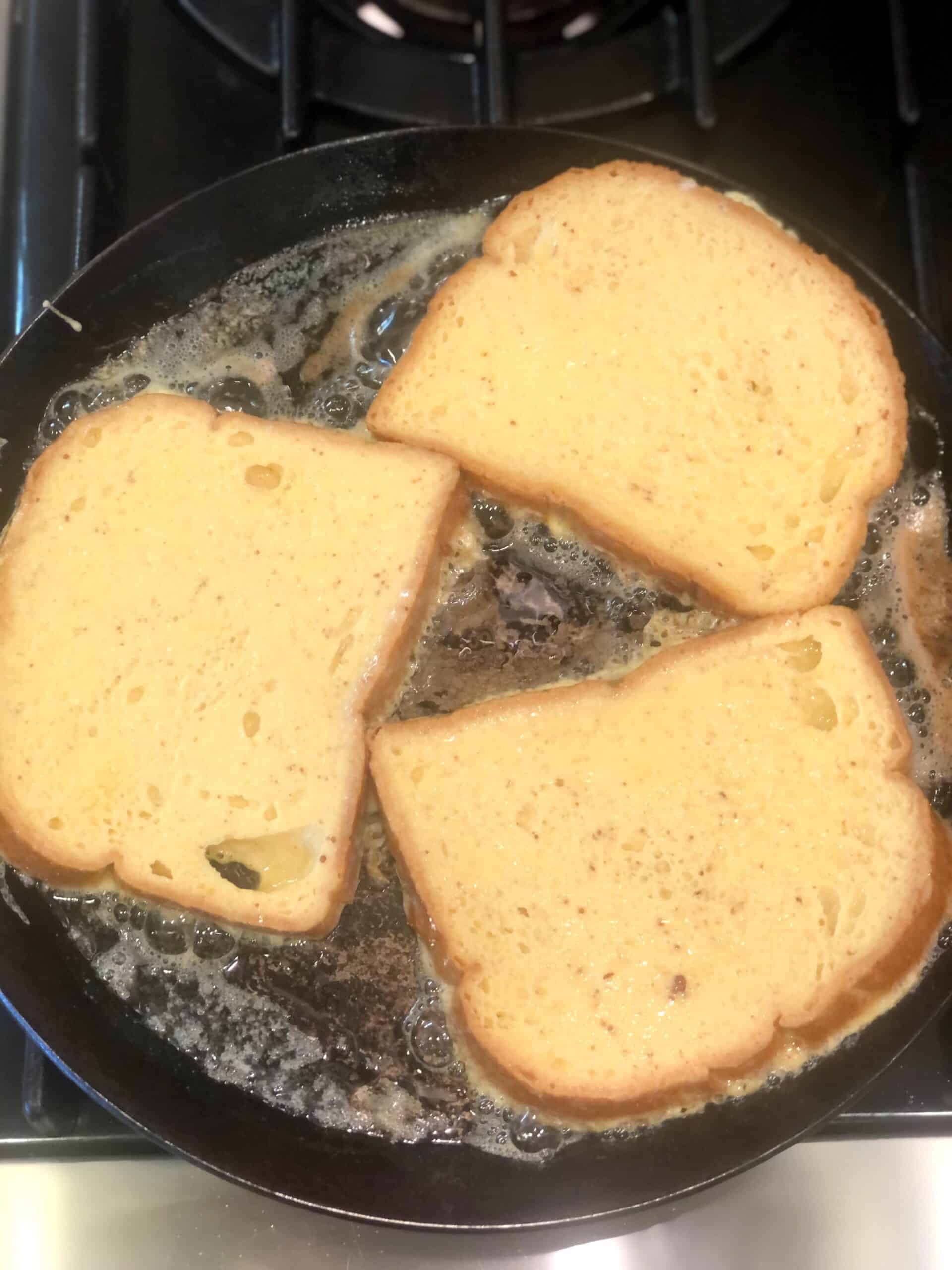 Three pieces of toast are being cooked in a pan on a stove.