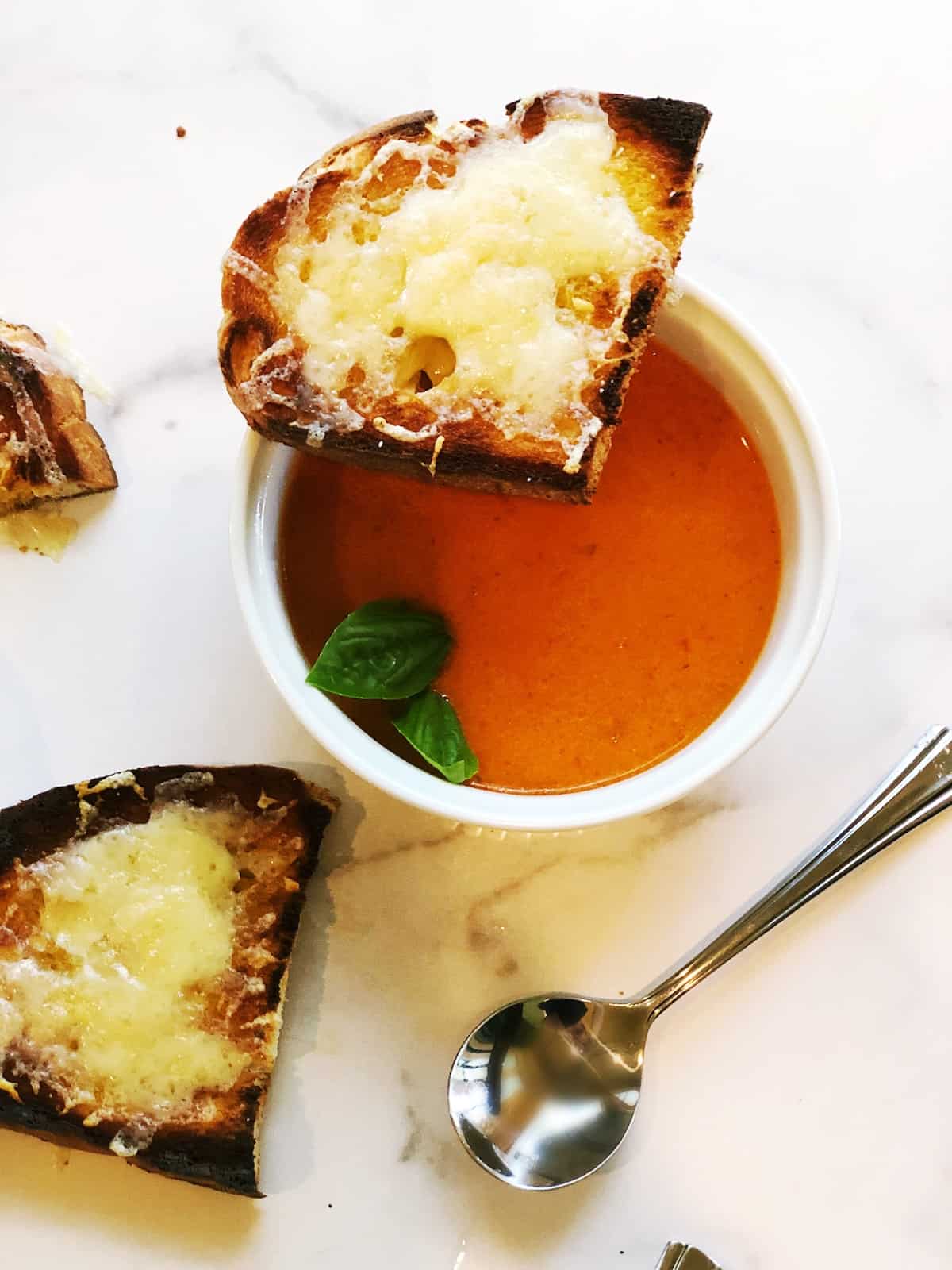 A bowl of tomato soup with bread and a spoon.