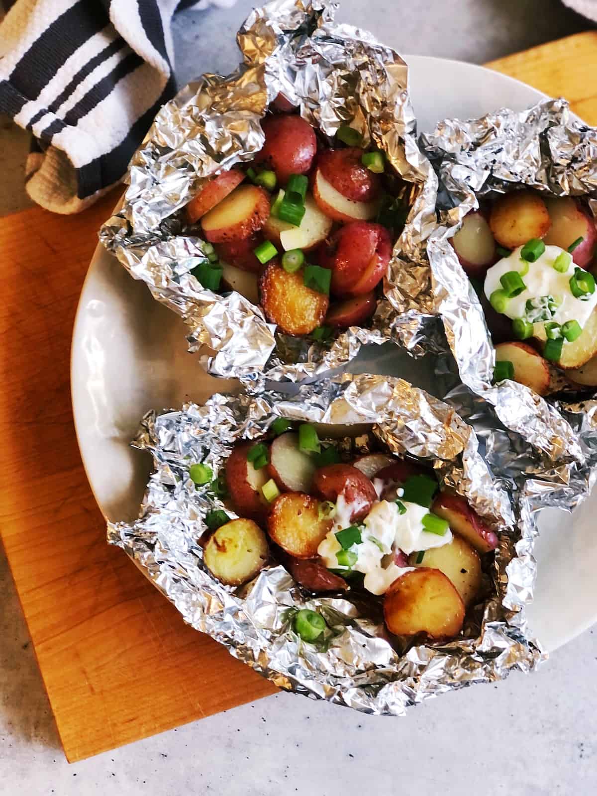 Potatoes in foil on a plate with sour cream and green onions.