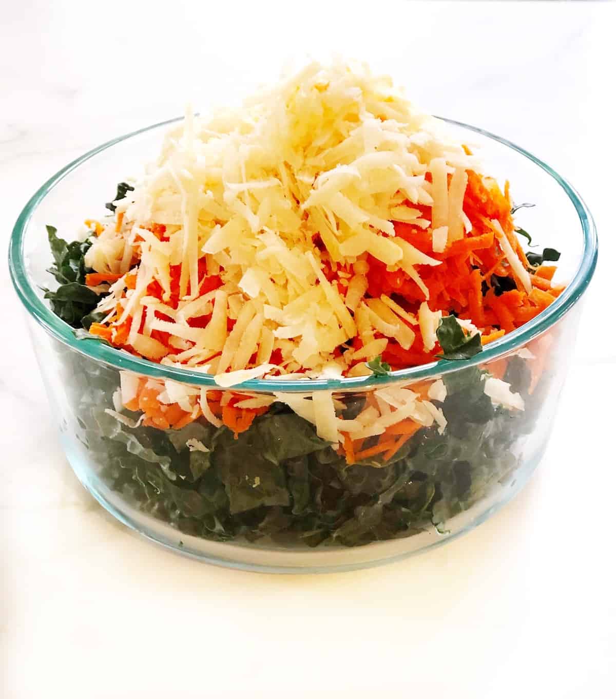 A bowl of kale salad with cheese and carrots.