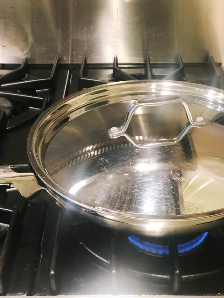 A stainless steel pan with a lid on top of a stove.
