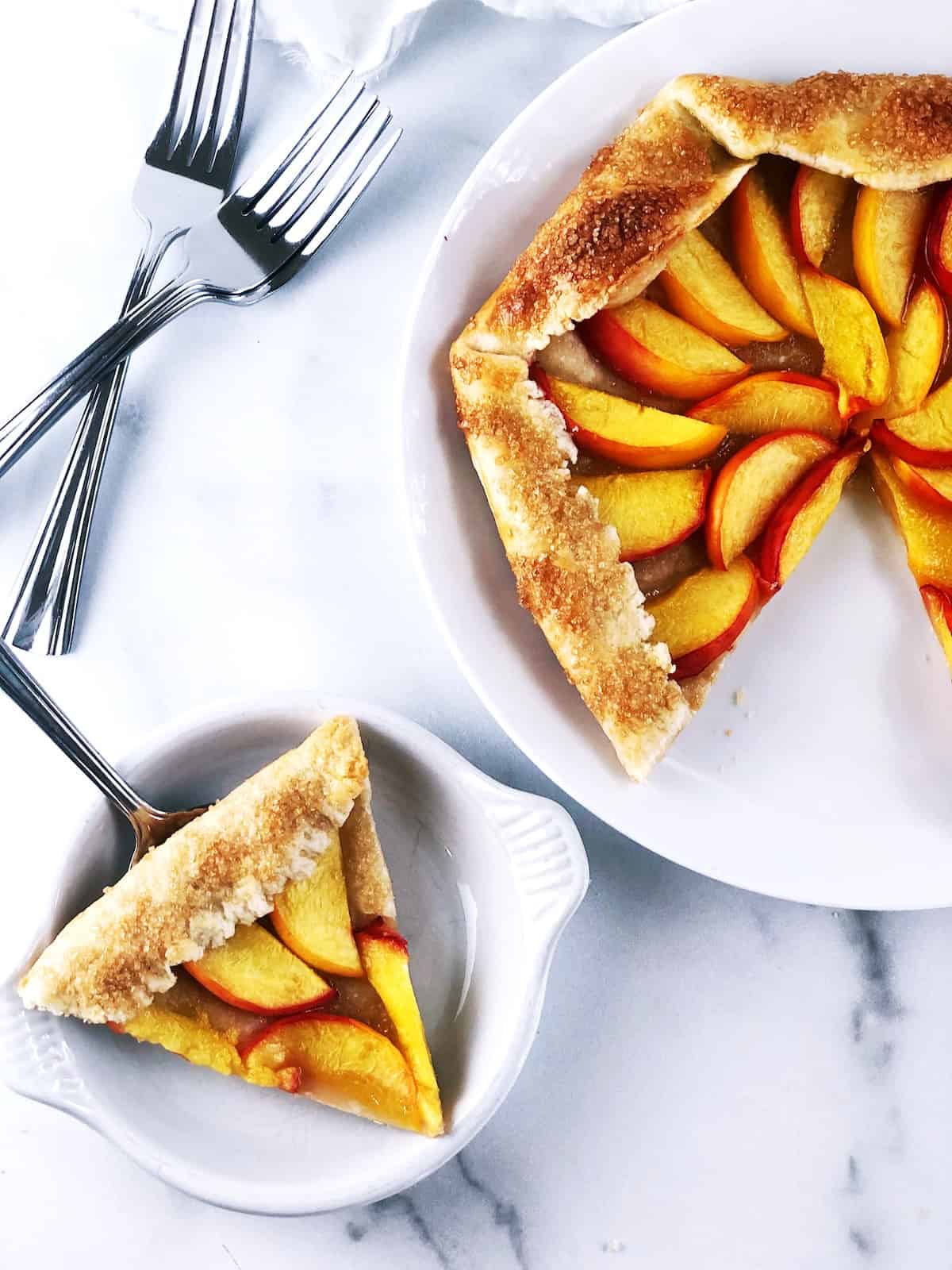 A slice of peach galette on a plate with a fork.