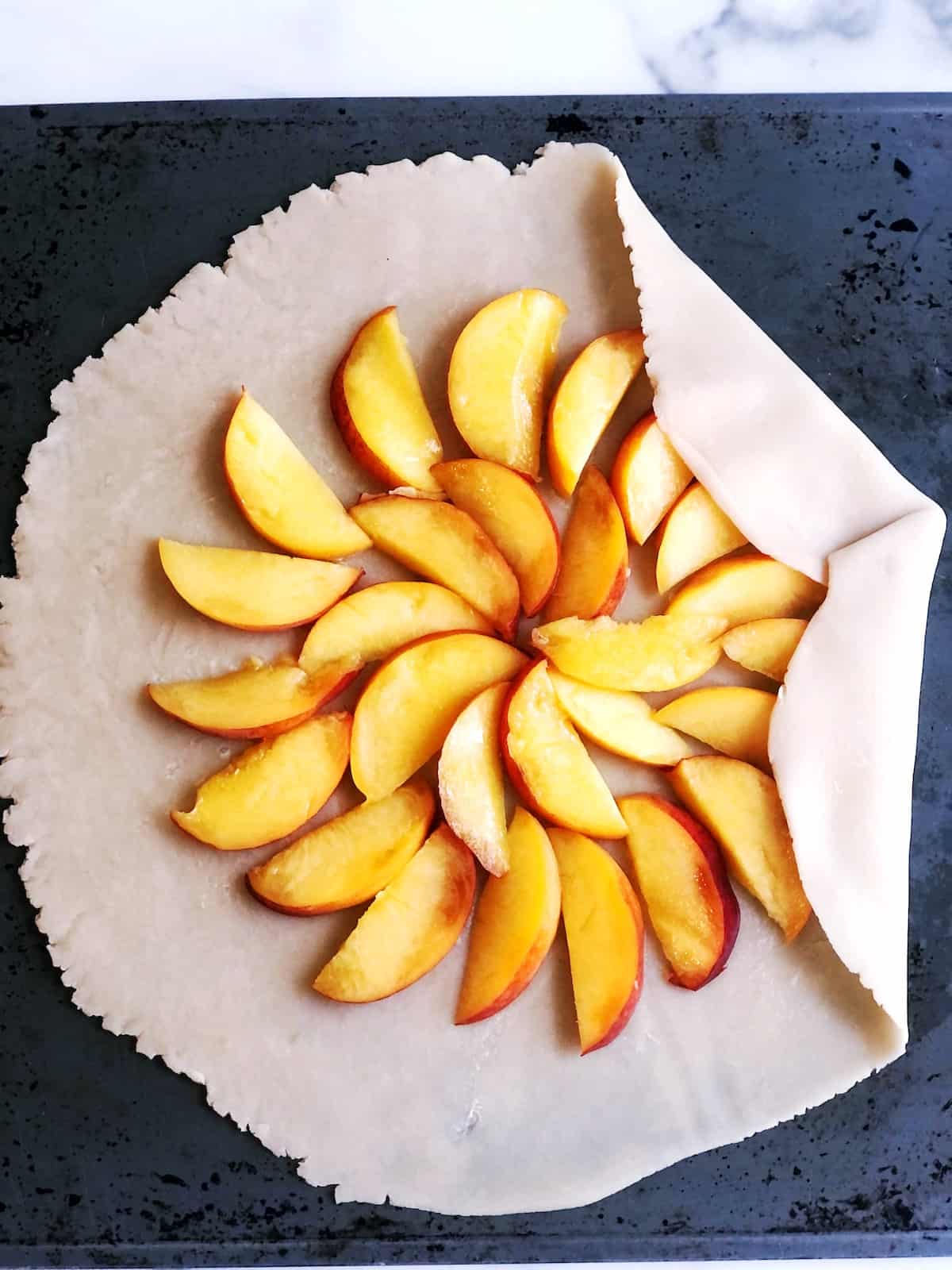 Sliced peaches on pie crust on a baking sheet.