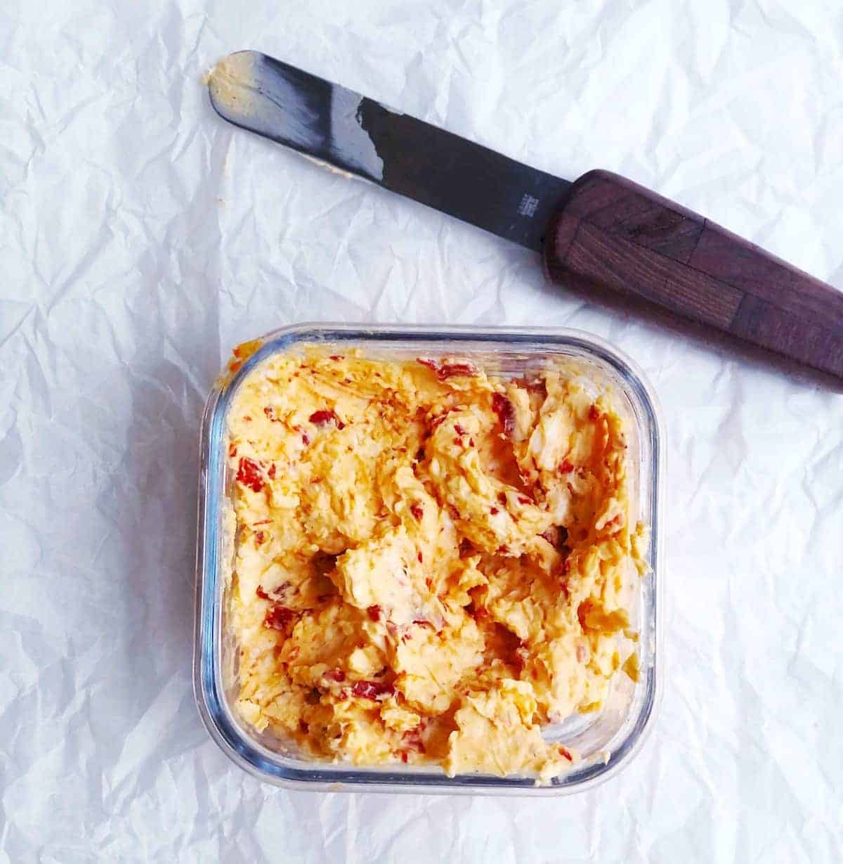 A plastic container with pimento cheese, and a knife next to it.