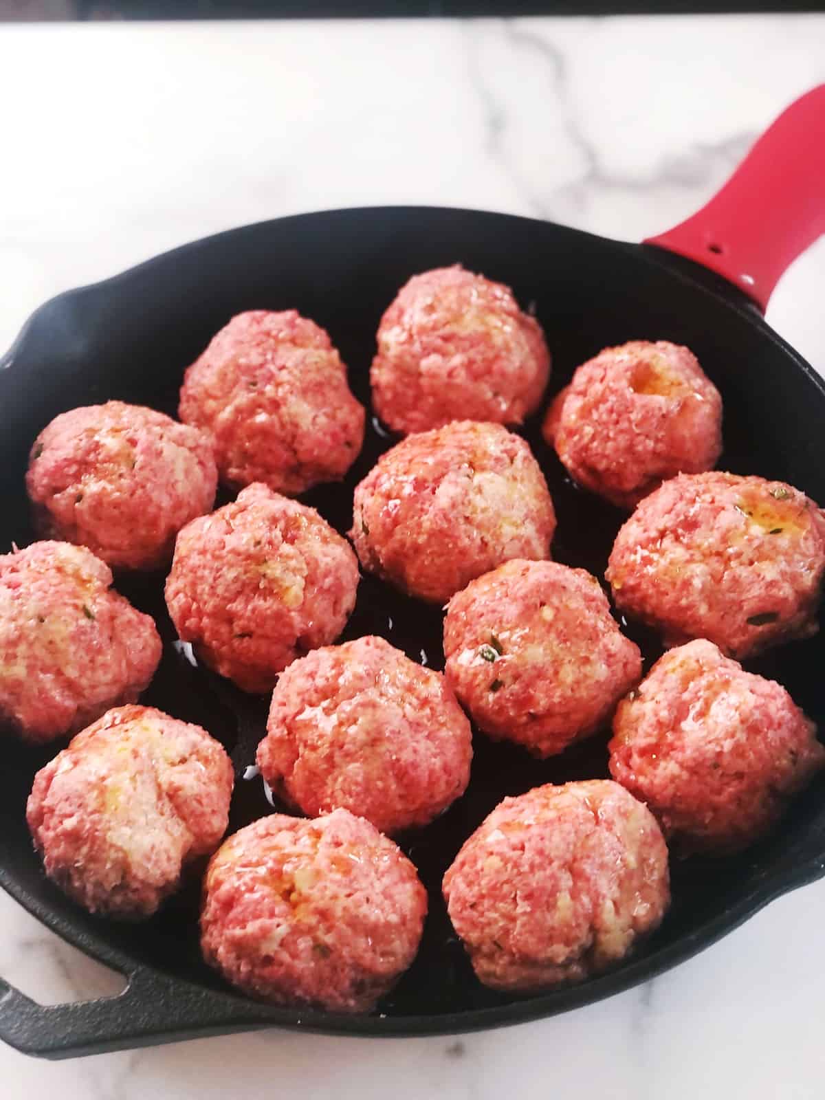 Meatballs in a skillet on a marble counter.