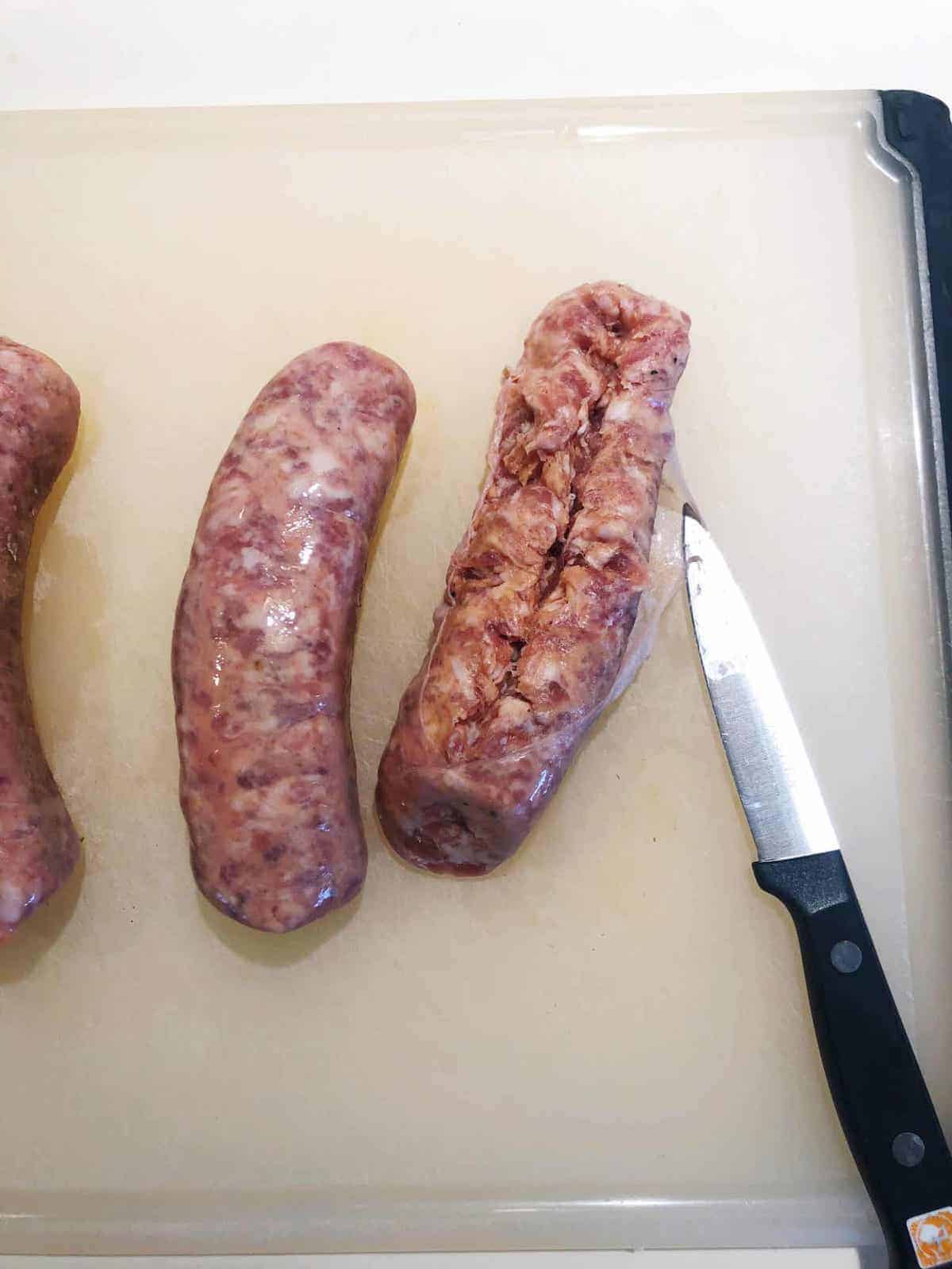 Three sausages on a cutting board with a knife.