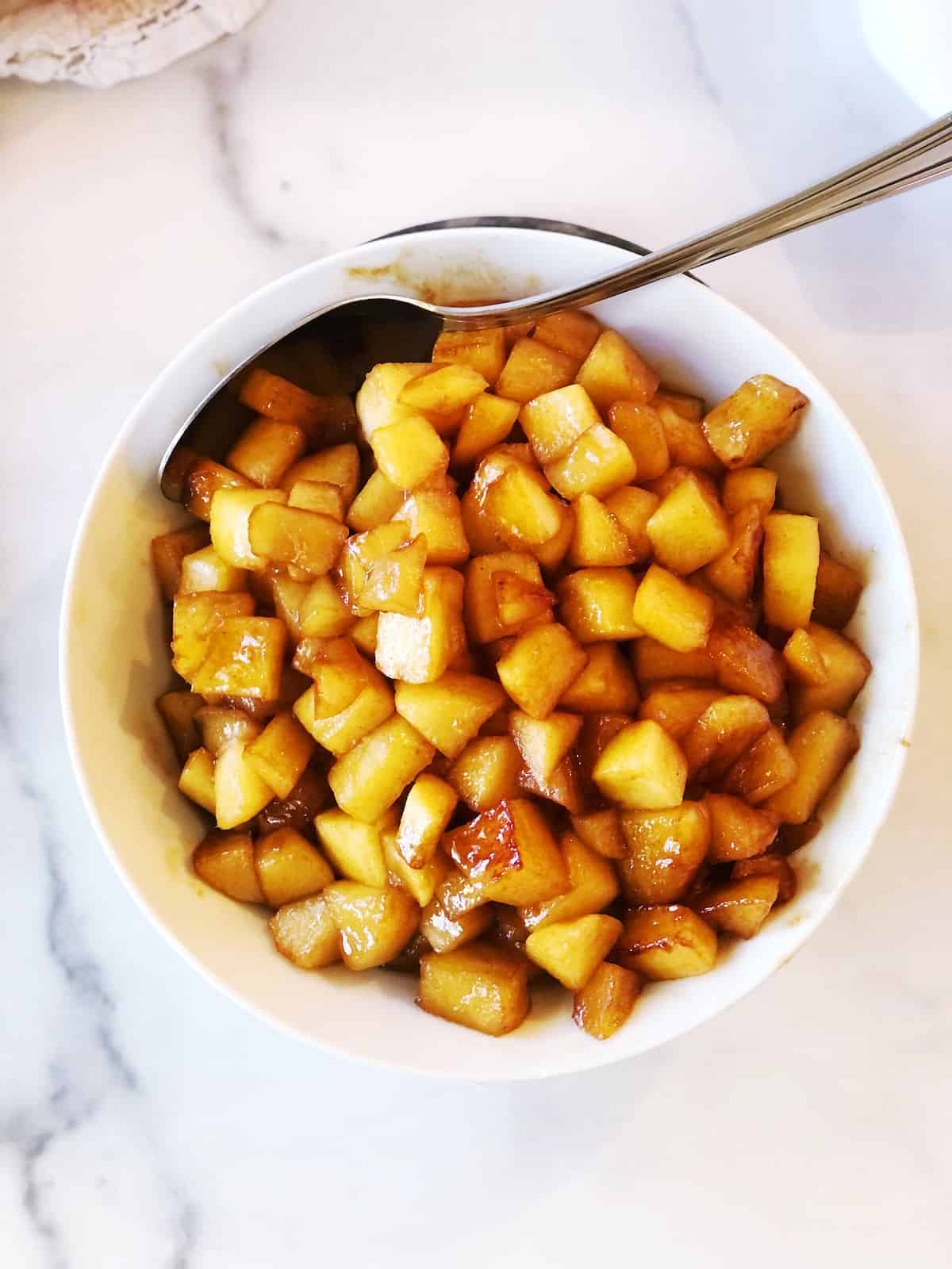 A white bowl with a spoon full of cubed apples.