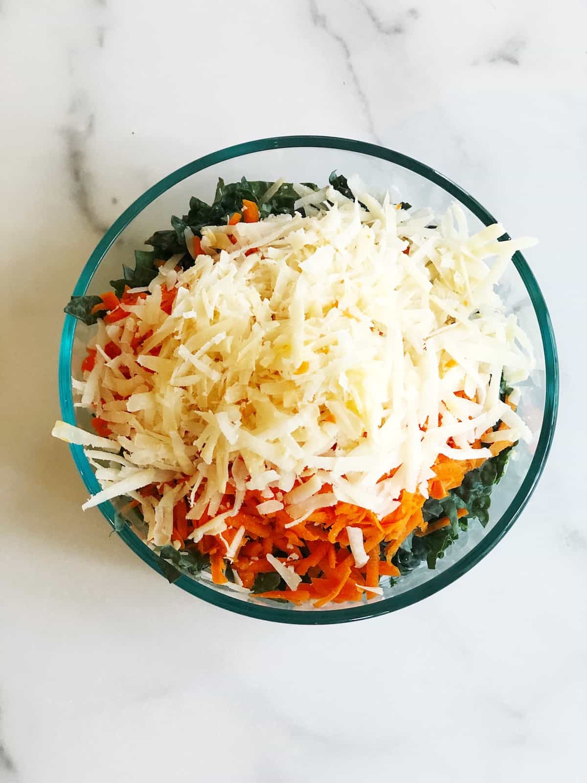 A bowl filled with carrots, kale, and shredded cheese.