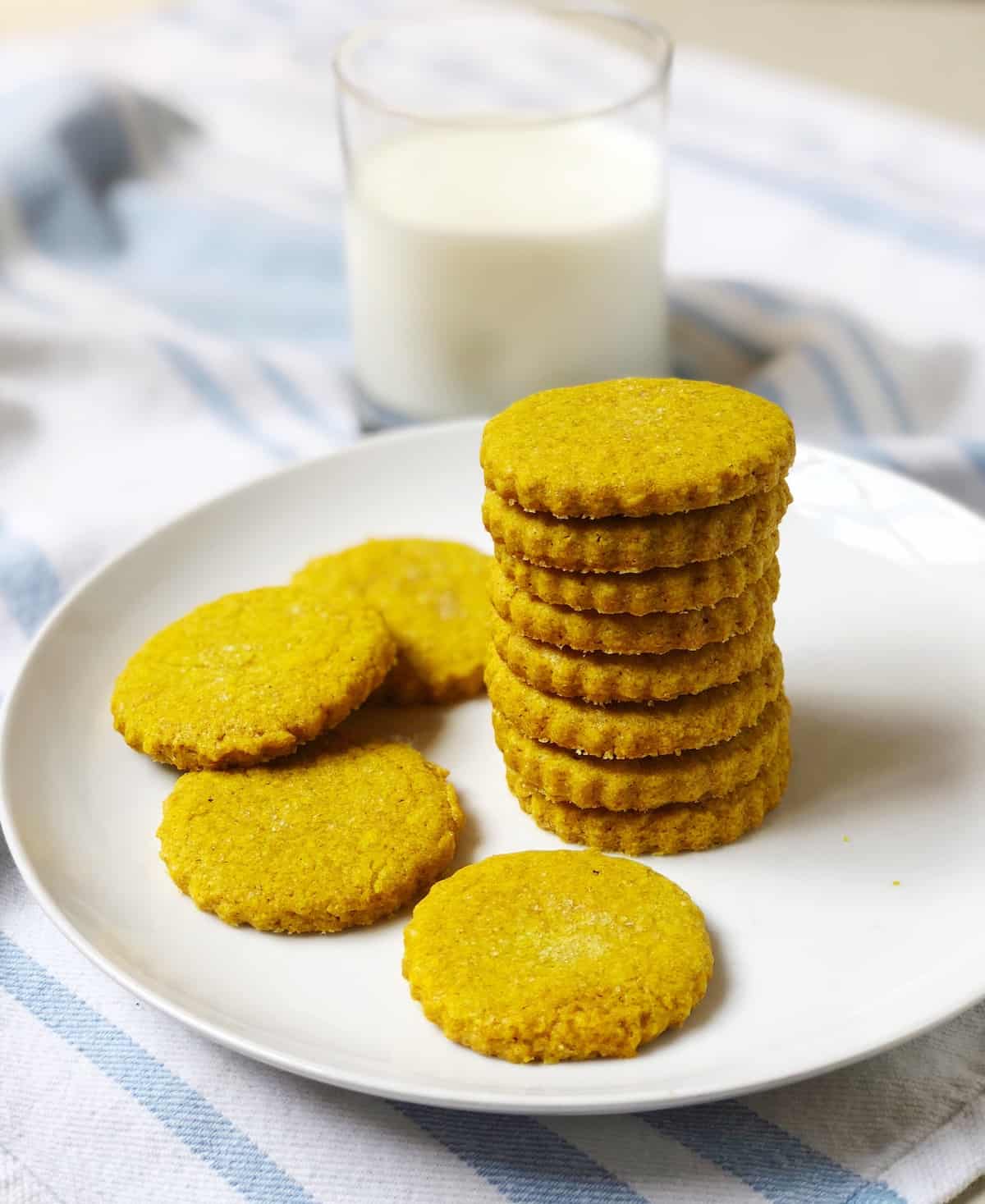 A stack of turmeric cookies on a plate next to a glass of milk.