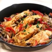 A skillet with Mediterranean salmon, onions and peppers.