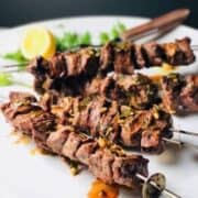 Grilled steak tips on skewers on a white plate.