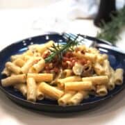 A plate of acorn squash pasta with mushrooms and sprigs of rosemary.