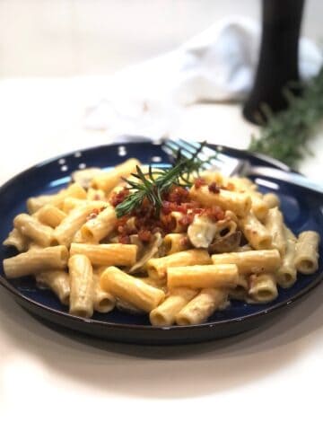 A plate of acorn squash pasta with mushrooms and sprigs of rosemary.