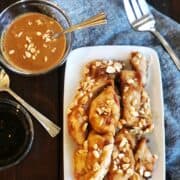 Baked chicken satay without skewers with peanut sauce on a white plate.