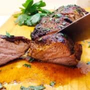 A knife is slicing a piece of pork tenderloin.