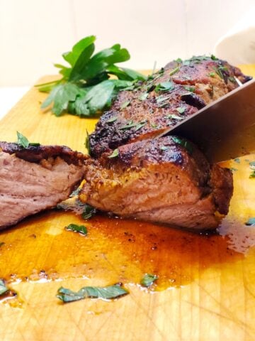 A knife is slicing a piece of pork tenderloin.