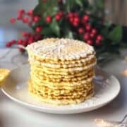 A stack of pizzelle with powdered sugar on top on a plate.
