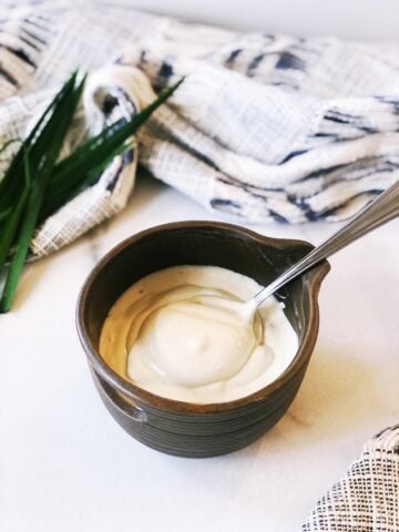 A bowl of tahini yogurt sauce with a spoon next to it.
