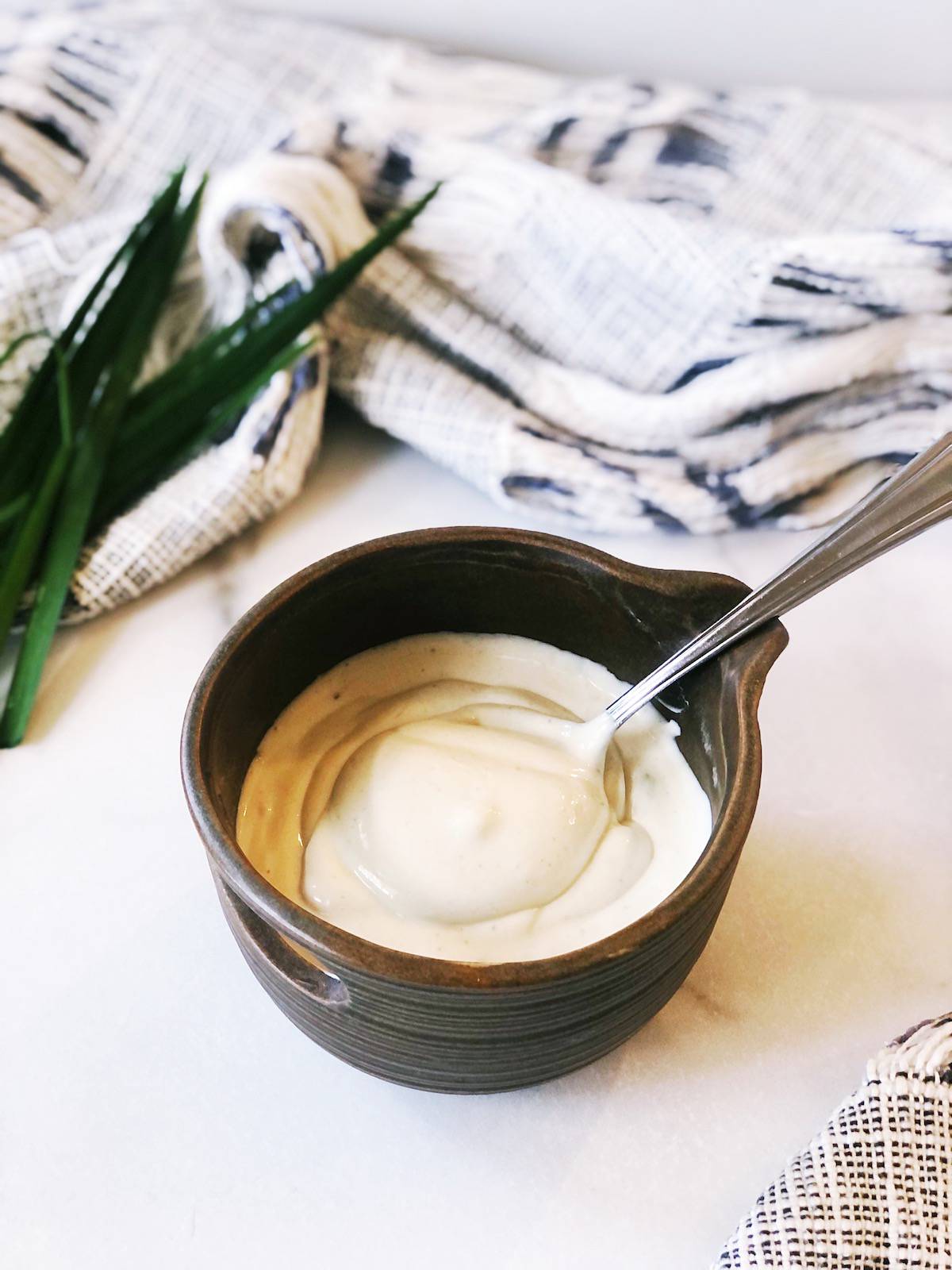 A bowl of tahini yogurt sauce with a spoon next to it.