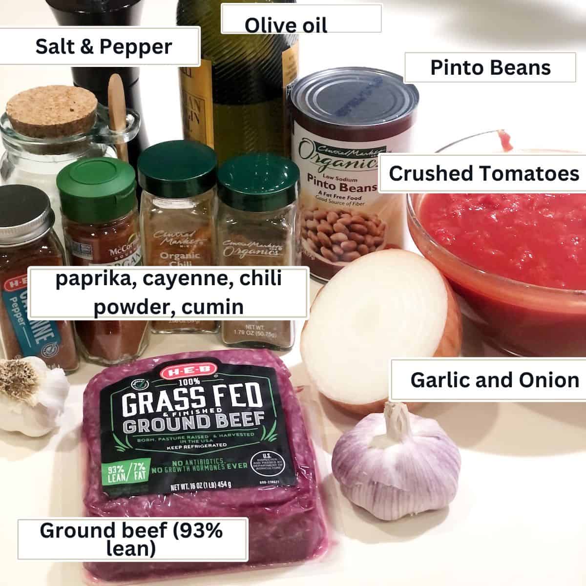 Dutch oven chili ingredients (ground beef, pinto beans, crushed tomatoes, onion, garlic, cumin, chili powder, paprika, salt, and cayenne pepper) on the counter.