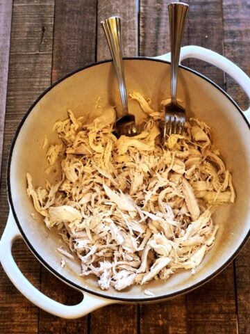 Shredded chicken in a Dutch oven with two forks.