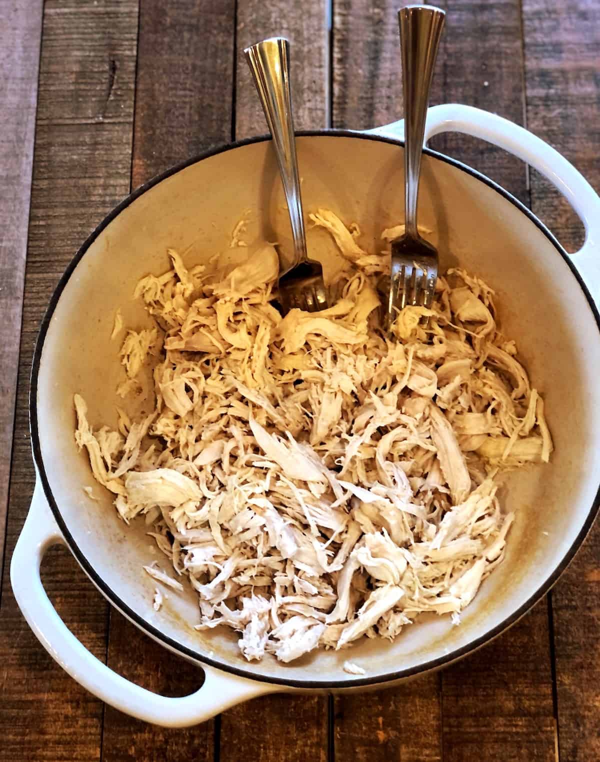 Shredded chicken in a Dutch oven with two forks.
