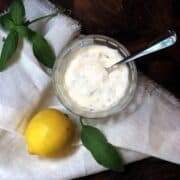 basil mayo in a bowl on a wood board with a lemon next to it.