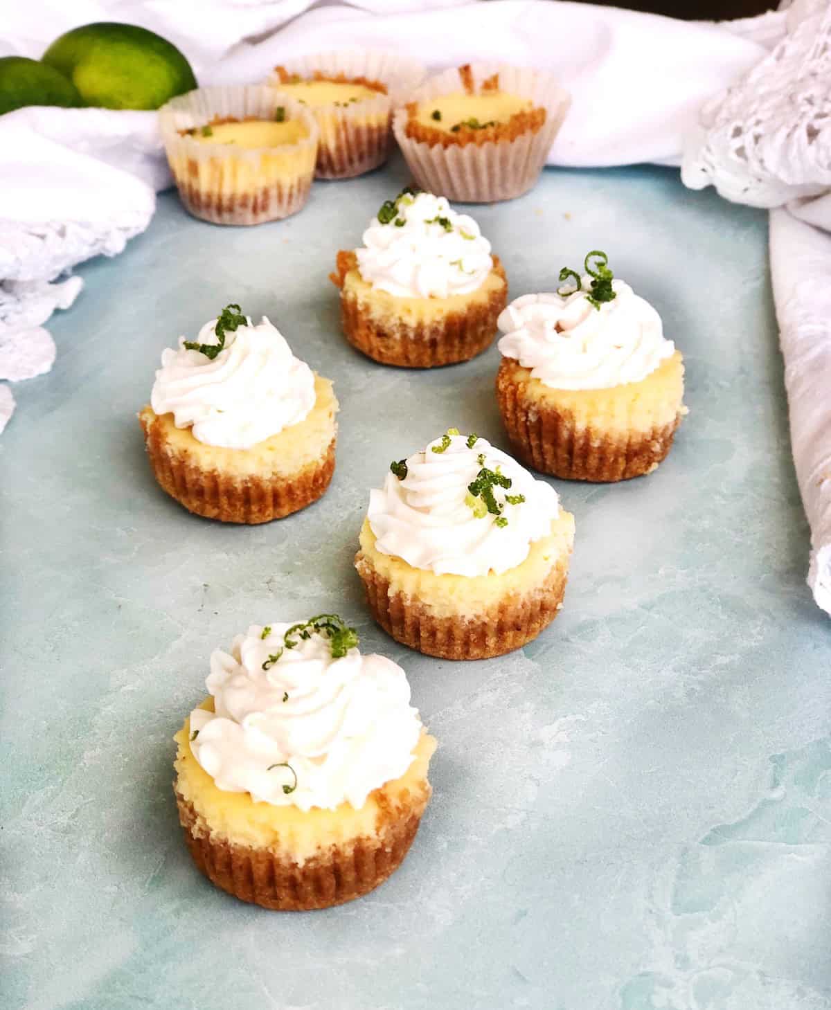 Mini Key Lime Cheesecakes with whipped cream on top on a blue counter.