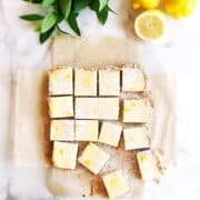 Sliced lemon bars on parchment paper with lemons next to it.