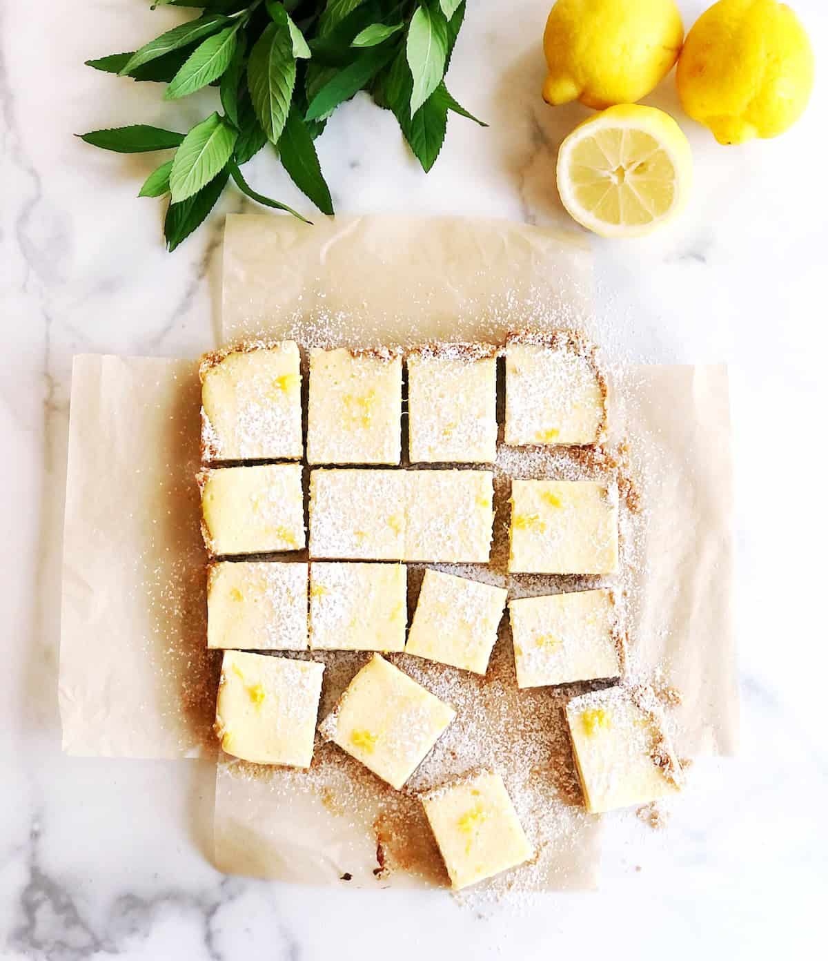 Sliced lemon bars on parchment paper with lemons next to it.