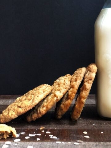 Oatmeal cookies stacked on their side on a wood board and leaning on a pint of milk.