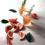 Two glasses of gin and tonic with grapefruit on a white board with multiple grapefruit wedges next to it.